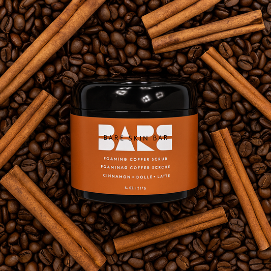 Bare Skin Bar foaming coffee scrub container surrounded by coffee beans and cinnamon sticks.
